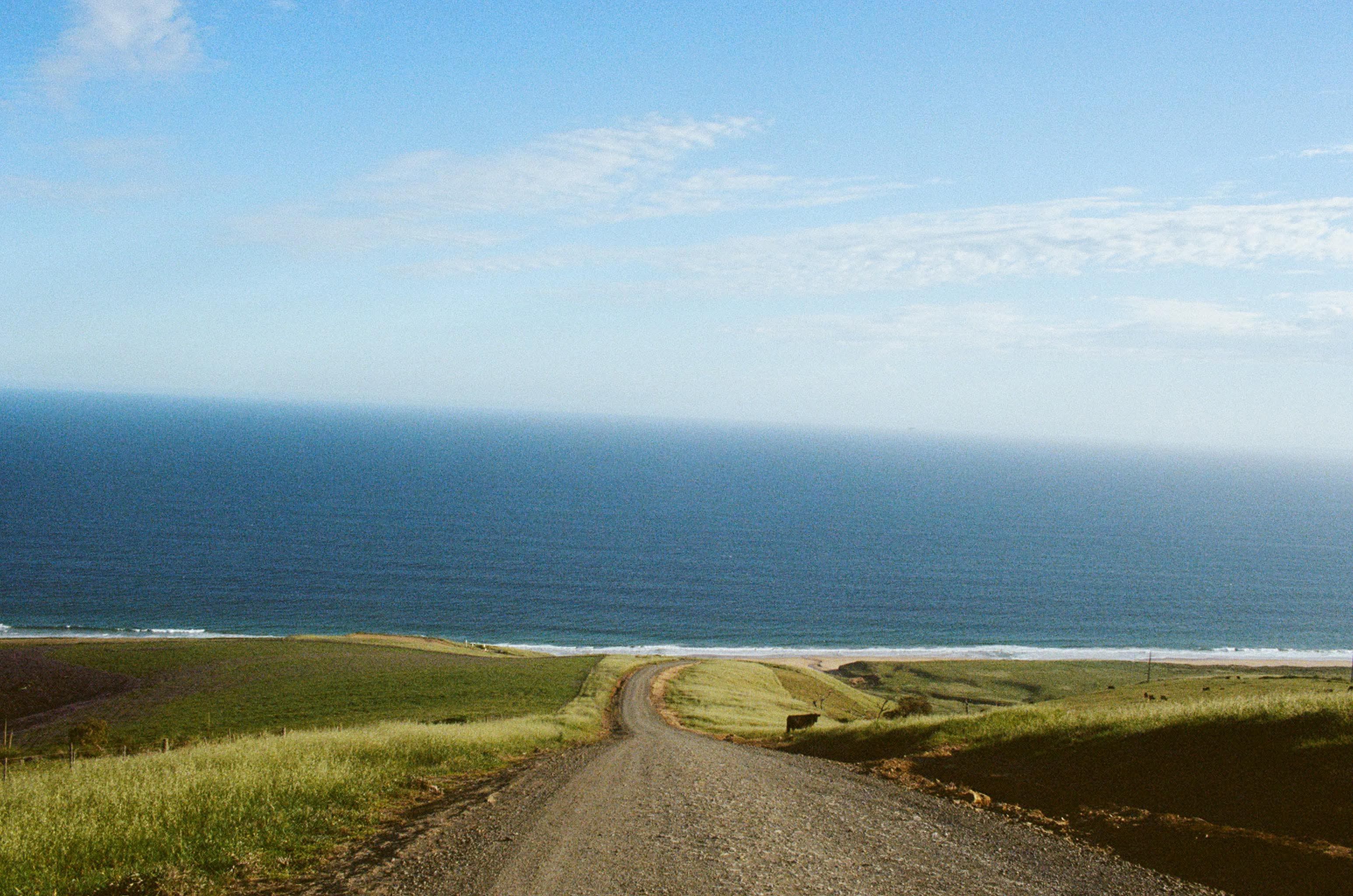 Gravel road leading to the ocean under a clear blue sky (KRAK SURF)